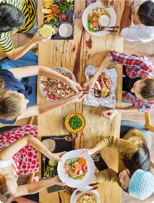 An aerial view captures various people around a table, sharing a meal—a reflection of the community and connection fostered by Cura, a proud member of the Elior North America family. This imagery resonates with Elior's commitment to excellence in food, service, and growth, highlighting the collective mission to serve healthy, delicious meals that enrich lives and enhance partner success.