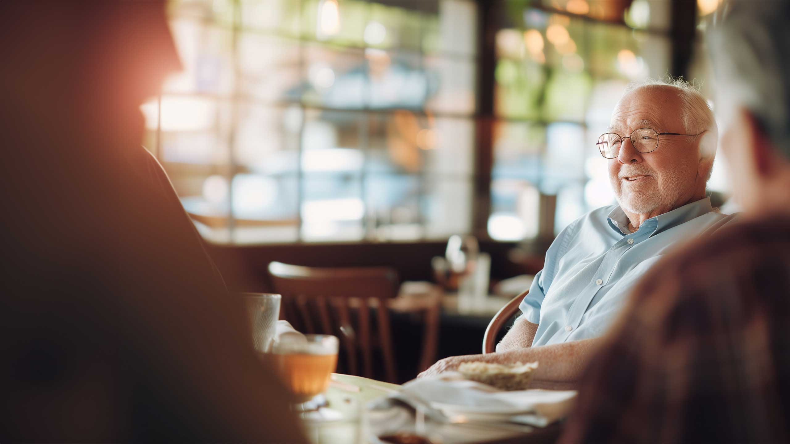 A senior gentleman engaging in conversation with friends over a meal in the communal dining area, reflecting the vibrant community spirit fostered by Cura Connect's senior living culinary programs.
